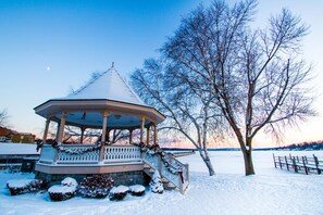 Ein Pavillon mit schneebedecktem Dach, umgeben von schneebedeckten Büschen und einem Baum.