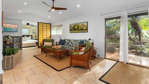 A spacious living room with a sofa, coffee table, and a dining area. There is a sliding glass door leading to a garden.