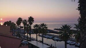 Marina con barcos amarrados, palmeras y un atardecer al fondo.