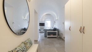 Un pasillo con un espejo grande, un banco y un sofá en una habitación moderna, bien iluminada, con paredes blancas y piso de baldosas.