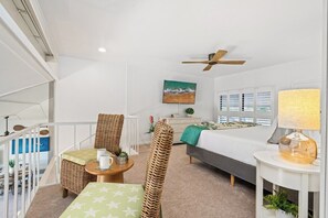A modern hotel room with a balcony, a bed with a green blanket, a round table with a cup and saucer, wicker chairs, and a ceiling fan. - Remodeled Beachfront 2BD w Year Round Beach - Maalaea Surf A6 (Kihei)