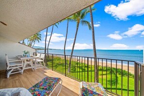 A balcony with a wooden floor, white furniture, and a view of the beach and ocean. - Remodeled Beachfront 2BD w Year Round Beach - Maalaea Surf A6 (Kihei)