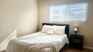 Een slaapkamer met een bed, nachtkastje, raam met zonwering en een radiator.