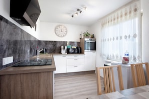 A modern kitchen with a built-in stove, a microwave, and an oven. There is a dining area with a wooden table and chairs. - Holiday Home 'Ayna' with Private Terrace, Private Garden and Wi-Fi (Bad Säckingen)