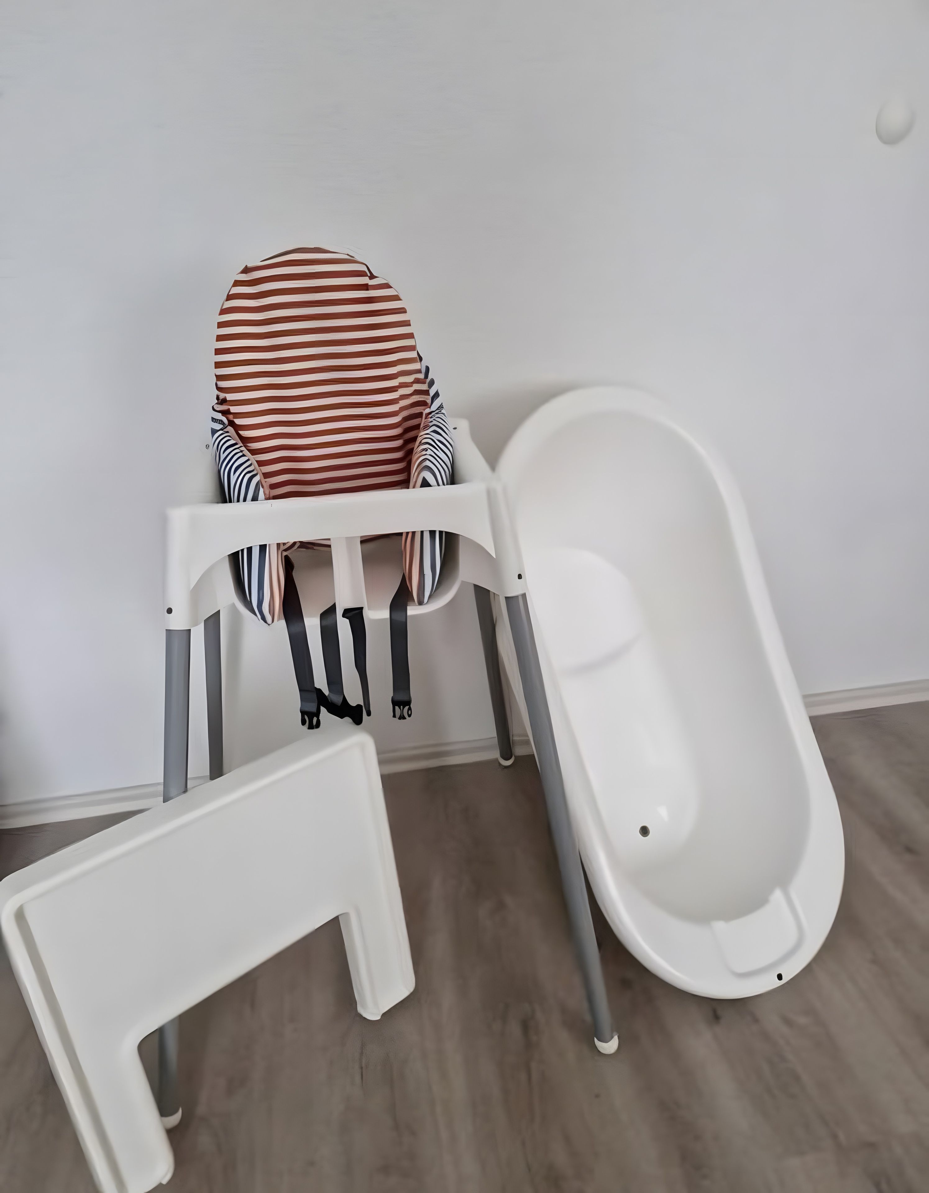 Une chaise haute pour bébé, de couleur blanche, avec un coussin à rayures et une baignoire blanche.