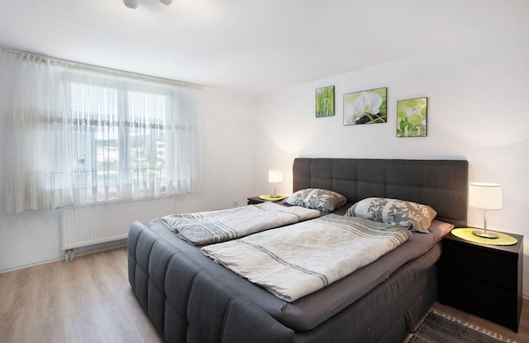 A bedroom with a bed, two bedside tables, a window with sheer curtains, and three wall-mounted pictures. - Holiday Home 'Ayna' with Private Terrace, Private Garden and Wi-Fi (Bad Säckingen)