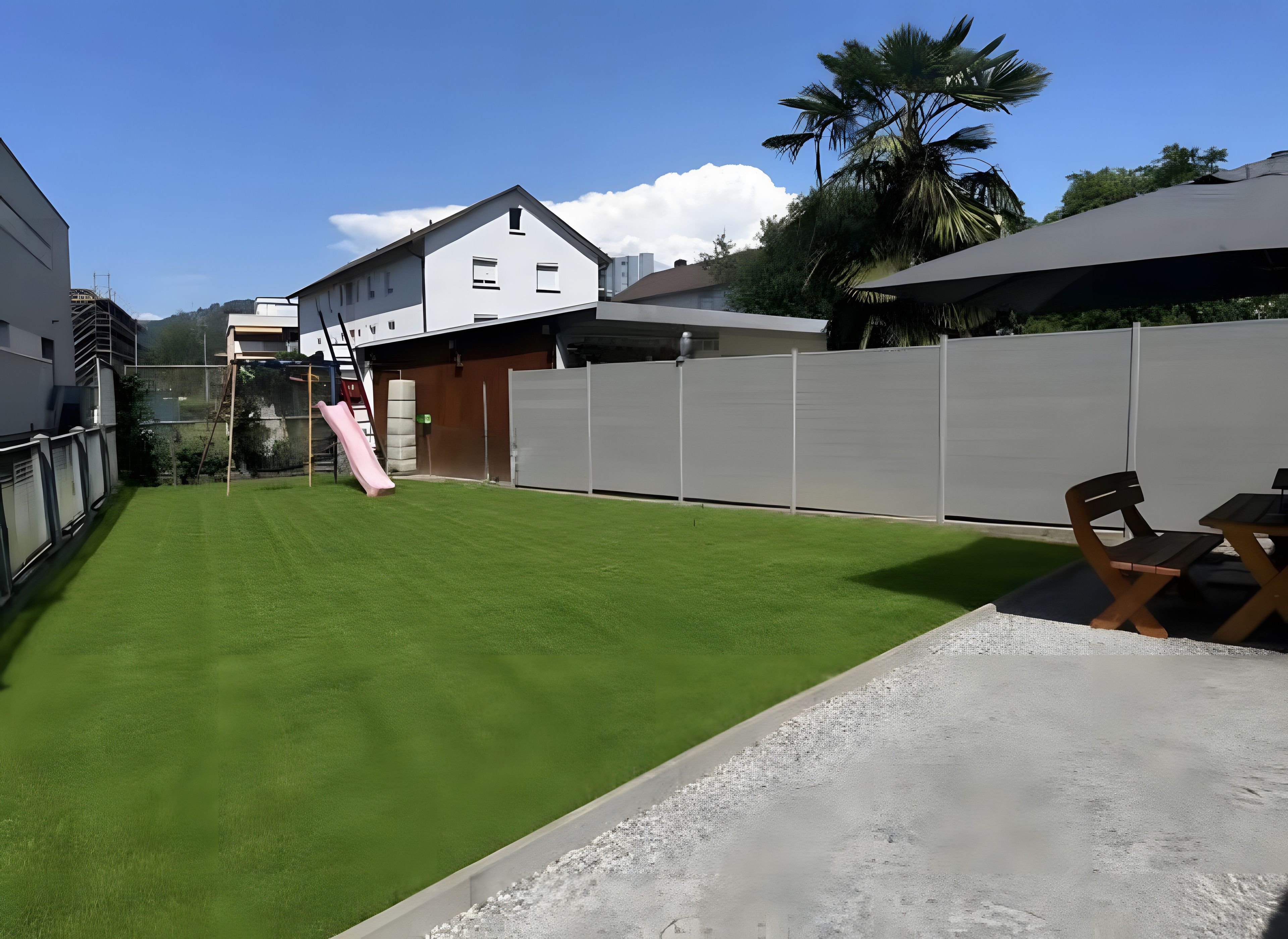 Ein Wohngarten mit einem grünen Rasen, einer rosa Rutsche und einem weißen Zaun.