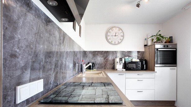 Eine moderne Küche mit Marmor-Spritzschutz, einer Holztischinsel, weißen Schränken, einer Uhr und einem eingebauten Backofen.