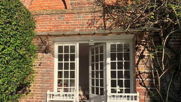 Un edificio de ladrillo con puerta y ventanas blancas, un pequeño porche y un seto.