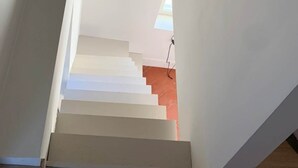Una escalera con escalones blancos que ascienden, una pared roja en la parte inferior y una ventana en la parte superior.