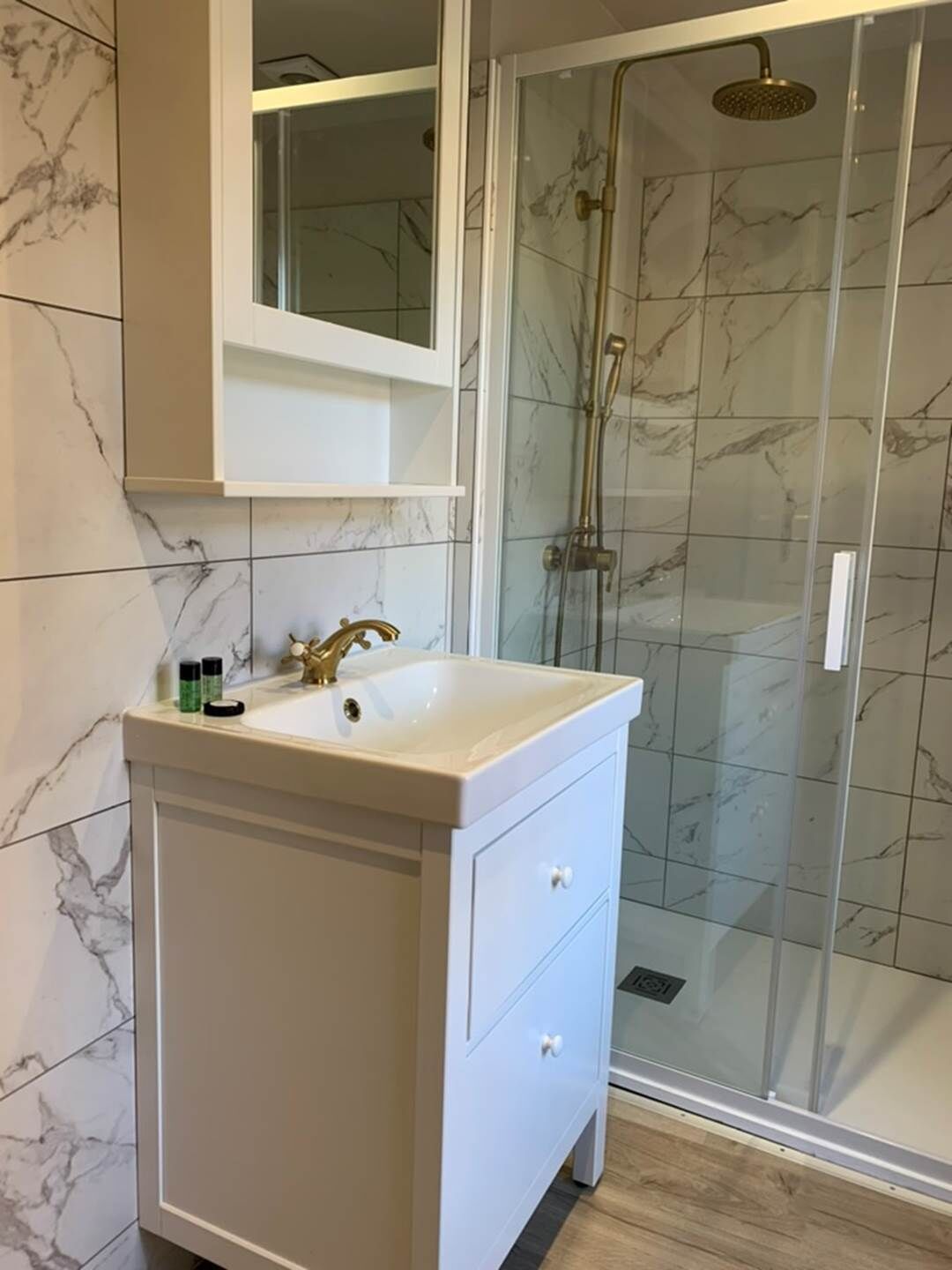 Baño con tocador blanco, cabina de ducha de vidrio y azulejos de mármol.