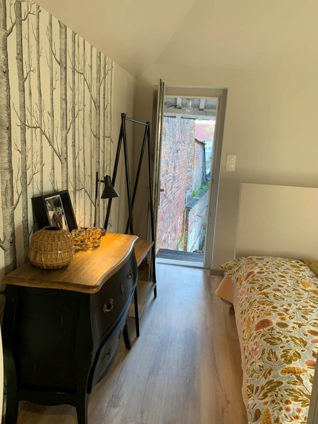 A bedroom with a bed, a dresser, a mirror, and a door leading to an outdoor area.