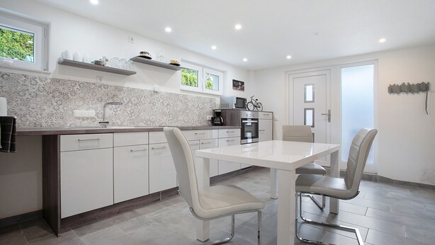 Une cuisine moderne avec des meubles blancs, une table à manger avec des chaises et un réfrigérateur.
