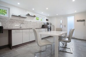 Uma cozinha moderna com armários brancos, uma mesa de jantar com cadeiras e uma geladeira.
