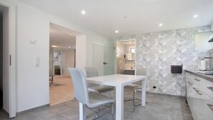 Une cuisine moderne avec une table et des chaises blanches, un pare-feu décoré et un grand miroir au-dessus de l’évier.