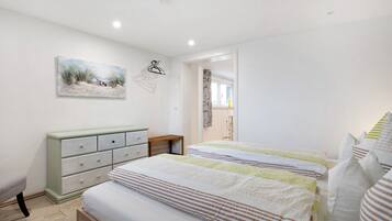 A bedroom with two beds, a dresser, a painting, and a door leading to another room.