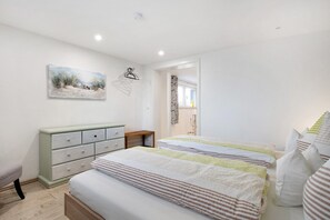 Quarto com duas camas, uma cômoda, um quadro e uma porta que dá para outro espaço.