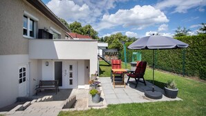 Une maison avec un patio, un banc, une table et un parasol.