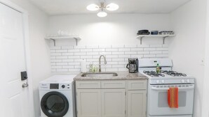 A compact kitchen with a washing machine, a sink, a stove, and a coffee maker.