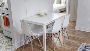 A modern kitchen with white cabinetry, a built-in stove, and a dining area with white chairs and a wooden table.