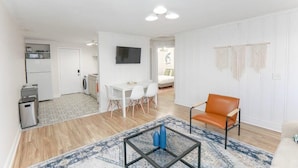 A modern living room with a glass coffee table, a sofa, and a dining area with chairs.