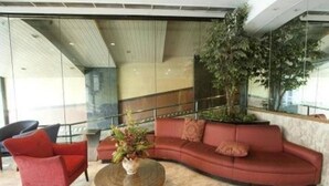 Een moderne lobby met een gebogen rode bank, een rond rieten bijzettafeltje en een grote kamerplant.
