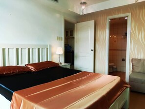 Relax in a spacious room with a large bed, a bedside table, and a door to a bathroom featuring a shower and toilet.