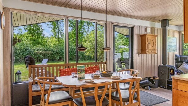 Un comedor de madera con una mesa y sillas, vista a zonas verdes exteriores y una cocina con estufa.