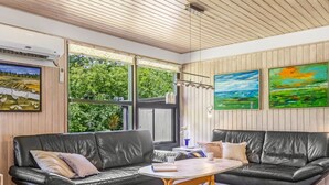 Una sala de estar moderna con un sofá seccional de cuero negro, una mesa de centro redonda y grandes ventanales con vistas al exterior.