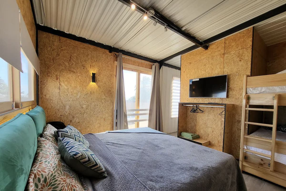 Quarto com uma cama, televisão fixada na parede e uma cama beliche de madeira.