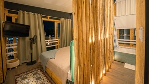 A bedroom with a bed, a TV, a fan, and a window with curtains.