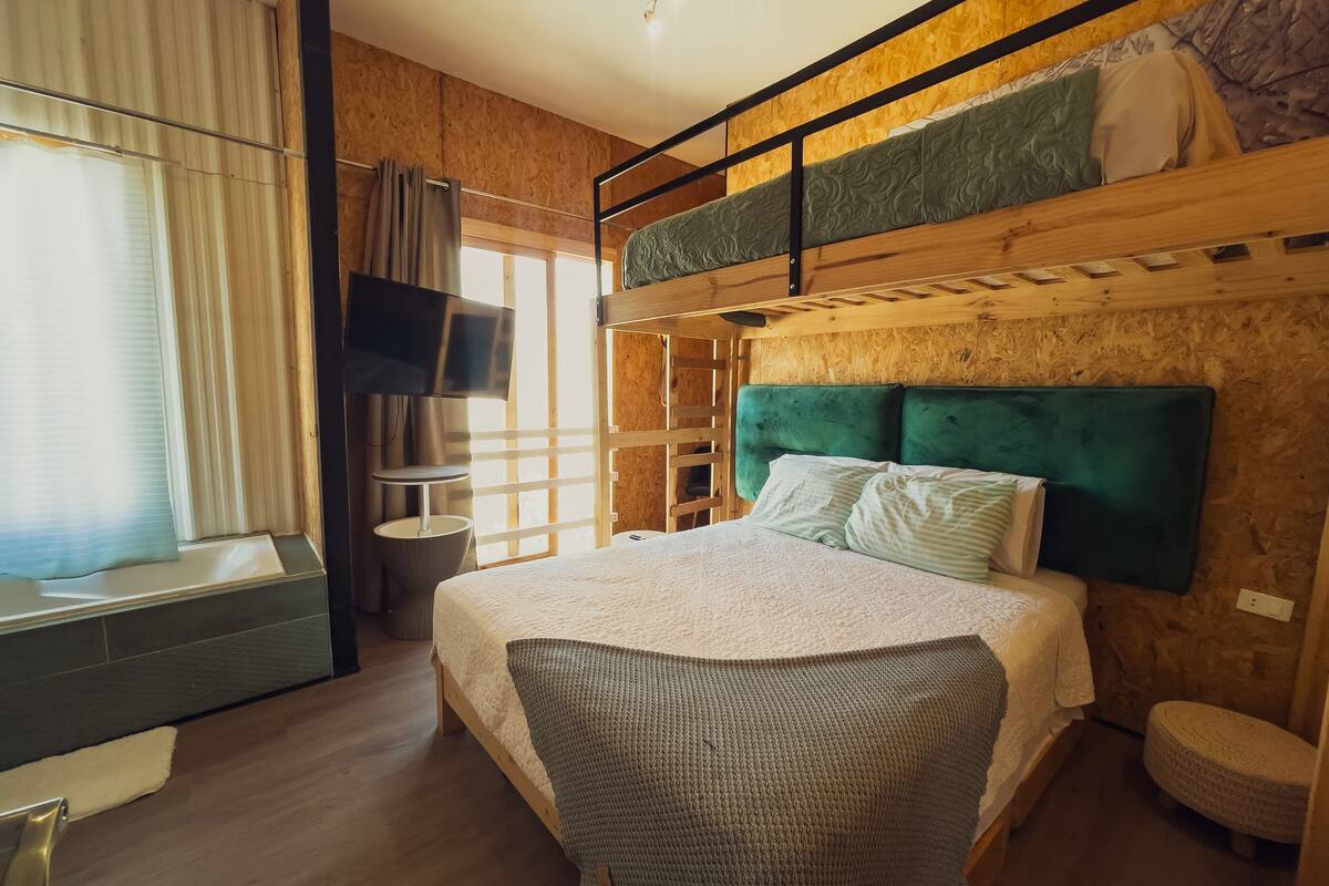 Quarto com beliche, televisão, uma mesinha e janela com cortinas.