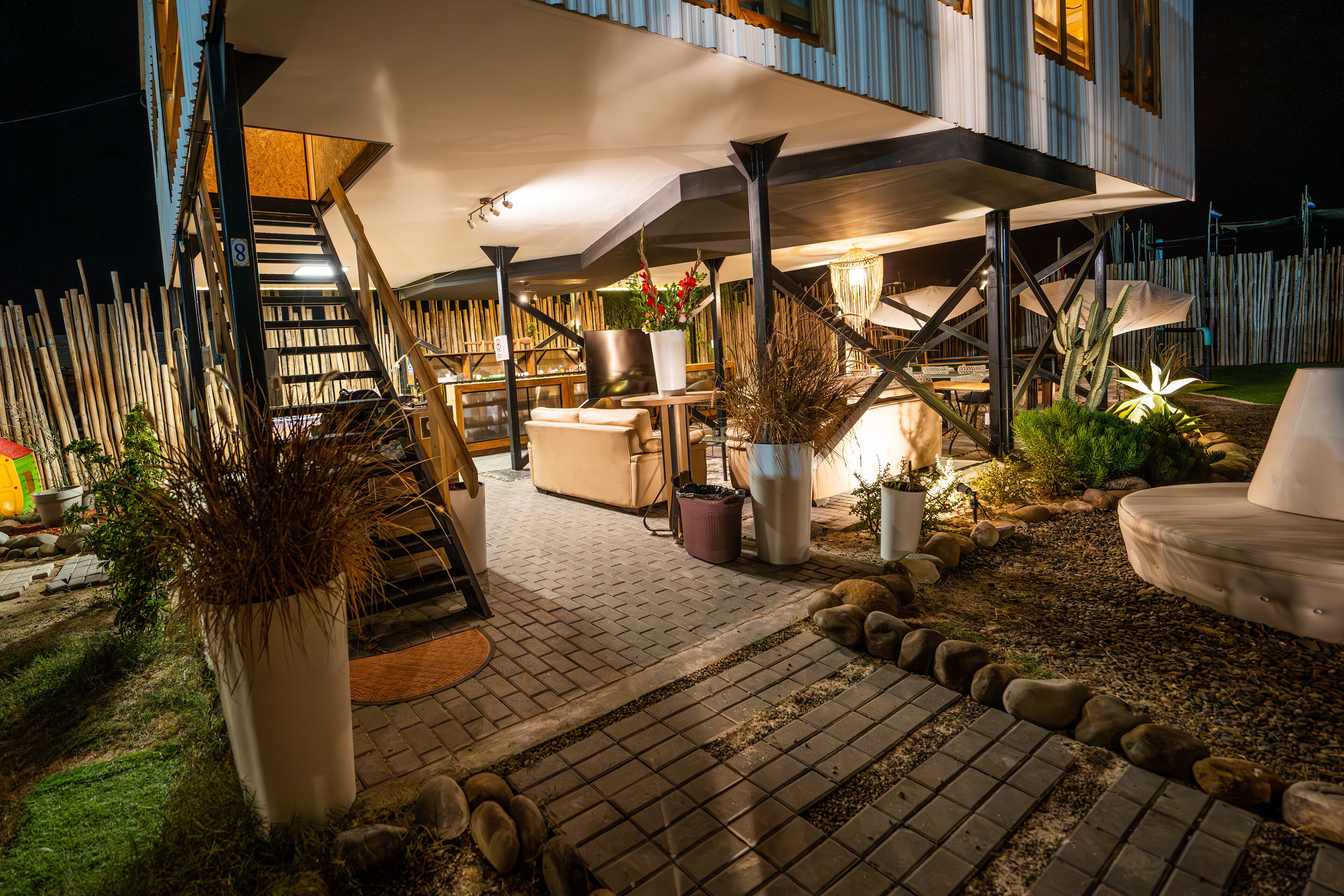 Un espace extérieur bien éclairé, avec une terrasse, un coin salon abrité, un escalier, ainsi qu’une variété de plantes et de meubles d’extérieur.