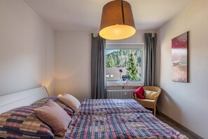 Une chambre à coucher avec un lit, une chaise, une fenêtre donnant sur des arbres et un luminaire suspendu.
