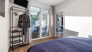 Hotelkamer met een bed, kledingrek, televisie en een glazen schuifdeur naar een balkon.