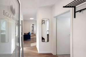Un couloir d’hôtel avec une porte en verre portant l’inscription « EGGE-RESORT », un miroir sur le mur et un canapé bleu en arrière-plan.
