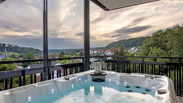 Een bubbelbad op een balkon met een prachtig uitzicht op een dorp en heuvels.