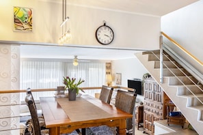 Un coin repas avec une table en bois, des chaises, une horloge et un escalier.