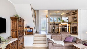 A living room with a wooden cabinet, a sofa, a staircase, and a dining area. - Edersee-Scheid Apartment with Lake View, Private Terrace & Wi-Fi (Waldeck-Scheid)