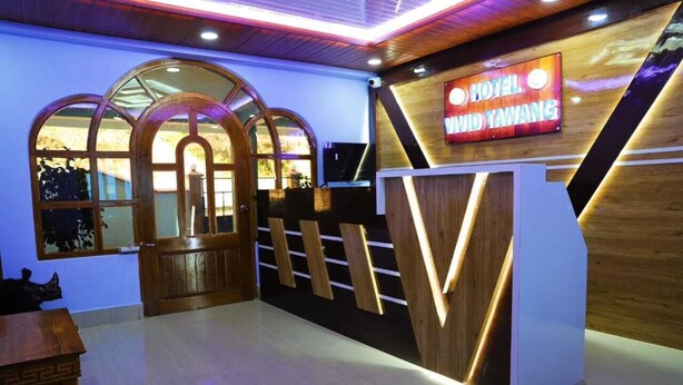 Un área de recepción con un mostrador de madera, un letrero de neón que dice 'Hotel David Tawang' y un gran ventanal en arco.