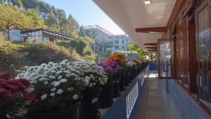 Un pasillo con una fila de macetas con flores, un muro de baldosas y un edificio con fachada de madera.