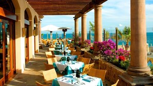 An outdoor dining area with tables and chairs, a wooden pergola, and a view of the ocean. - Oceanview 2BR/2BA Presidential Suite at Sunset Beach Oceanfront Resort, Golf Spa (Cabo San Lucas)