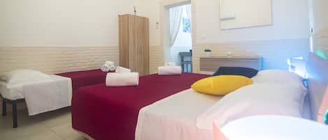 A hotel room with two beds, a wooden wardrobe, a small table, and a mirror on the wall.