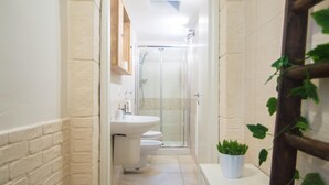 A narrow bathroom with a white sink, toilet, and glass-enclosed shower. - Casa Camerini in Villanova (Ostuni)