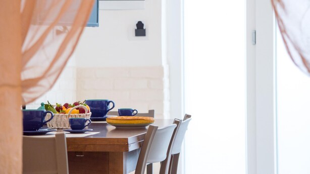 A dining table with a basket of fruit, a pie, and blue cups. - Casa Camerini in Villanova (Ostuni)