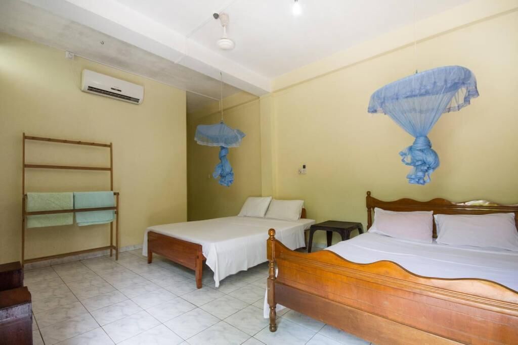 A room with two beds, a wooden bench, a small table, and a hanging blue canopy.