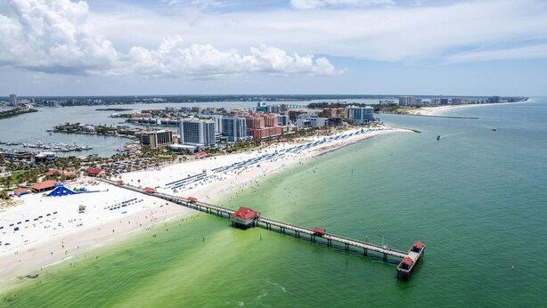 A coastal cityscape with a long pier extending into the ocean, a sandy beach, and a marina with boats. - The Cottage in Clearwater - 30 Day Minimum Stay (Clearwater)