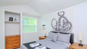 A bedroom with a bed, a dresser, a window with blinds, a wall mural, and bedside lamps. - The Cottage in Clearwater - 30 Day Minimum Stay (Clearwater)