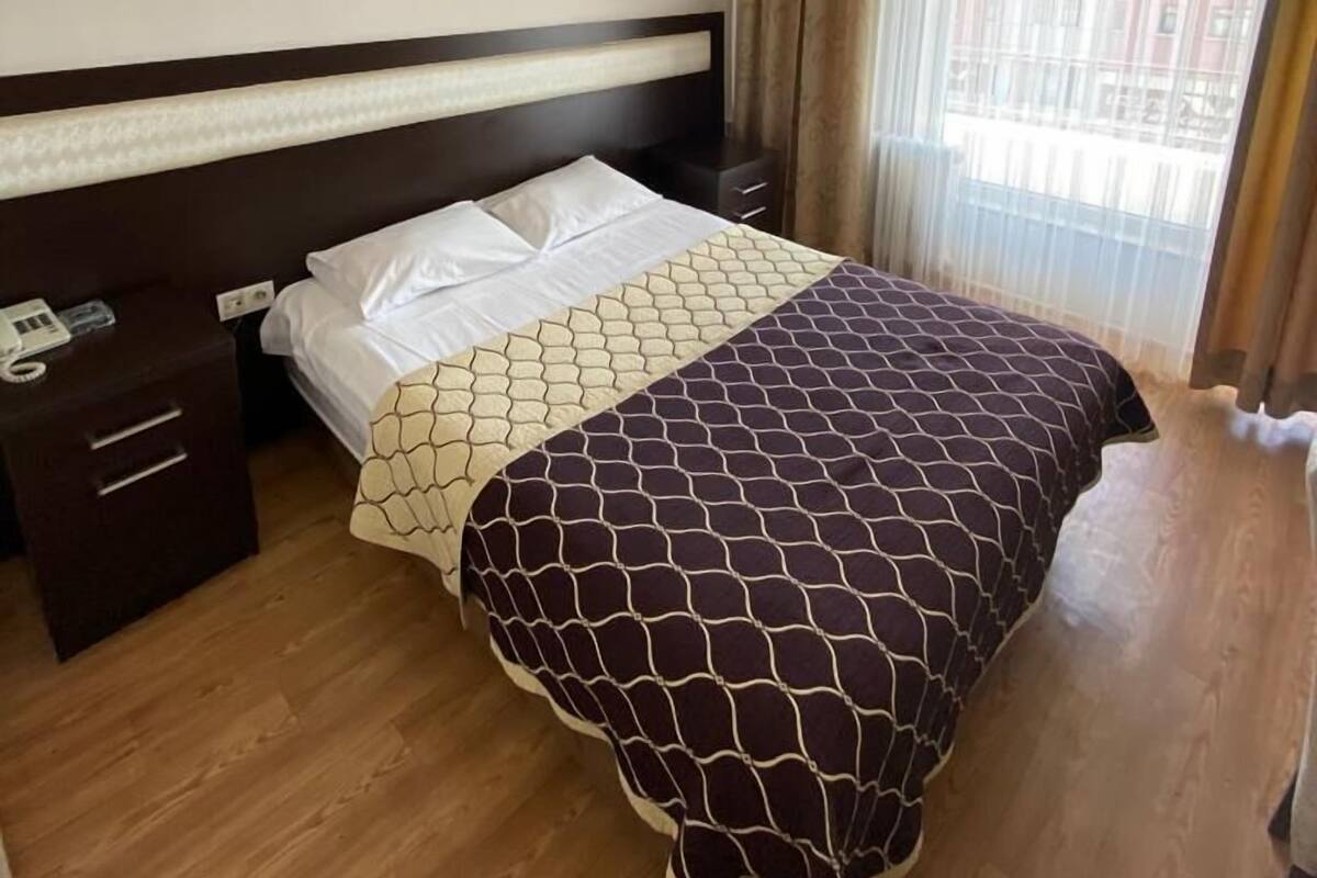 Quarto de hotel com cama, mesa de cabeceira, ventilador de teto e janela com cortinas.