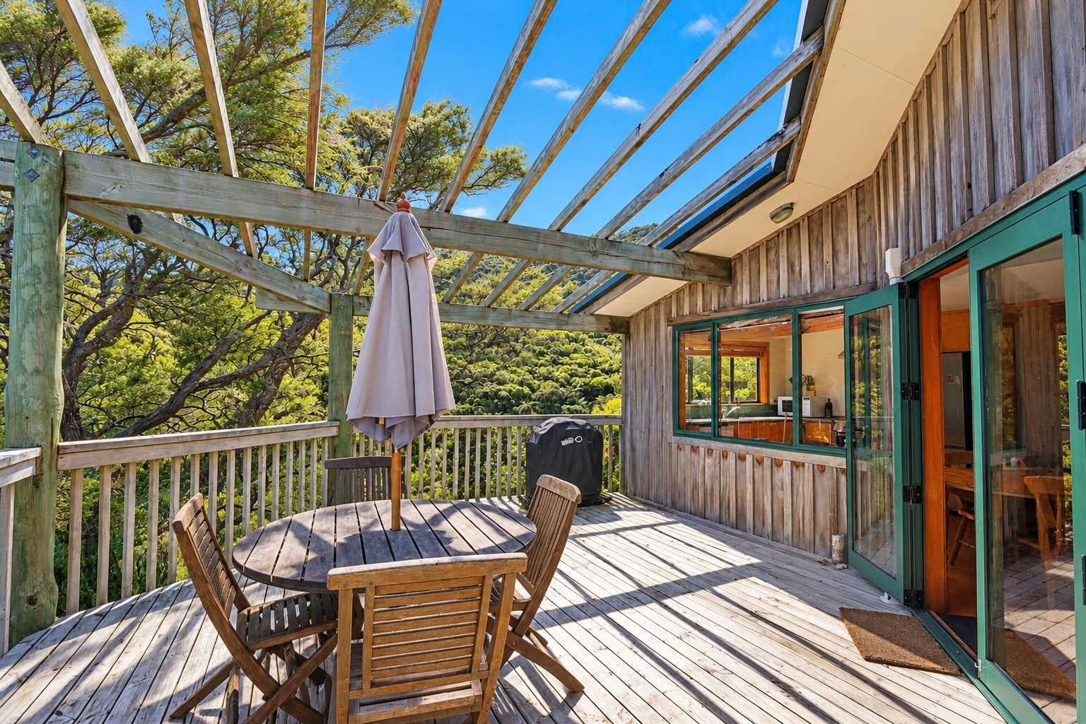 A wooden deck with a table and chairs, a covered umbrella, and a view of the surrounding trees.